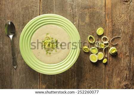 Top view of a bowl of leek soup with fresh leek rings on a wooden background