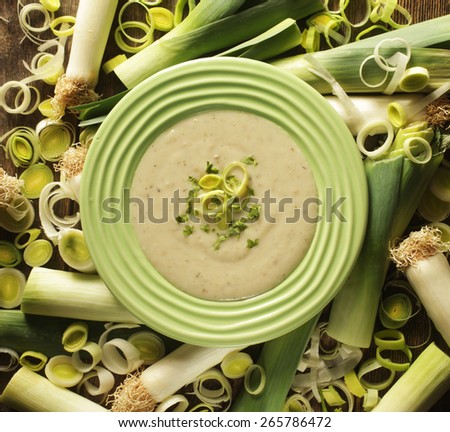 Top view of a leek soup in a green bowl surrounded by fresh leek.
