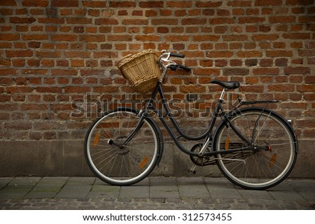 Black bicycle with straw basket along a brick wall