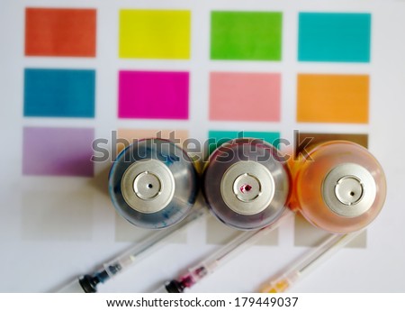 Bottle of ink printer has three colors. Colors is red, yellow and blue with syringe on colored paper.