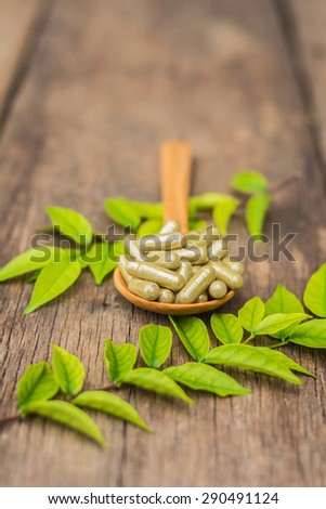 Herbal medicine capsules in spoon with leaf of plant on old wooden background