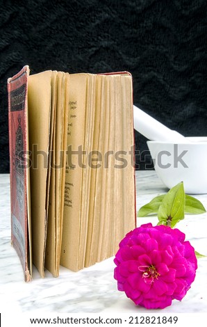 Old book with red binding and flower on a marble table