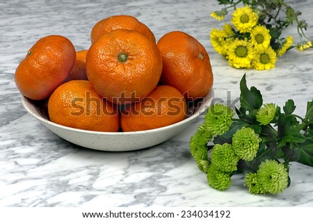 Tangerines on a plate with green and yellow gerber on a marble table