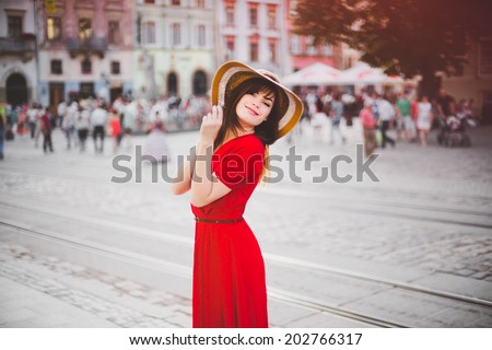 a happy girl in a red dress and widebrimmed hat in the city-center