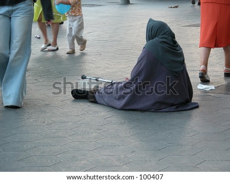 Begging woman with people walking by in the streets of Barcelona, Spain