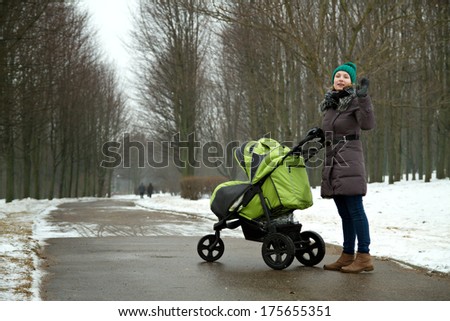young mother with a stroller on a walk in winter park