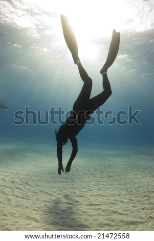 A freediver descends to the ocean floor as the sun streaks beams of light from the surface of the ocean