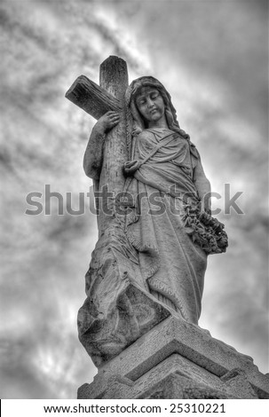 Madonna statue leaning against a cross adorning tomb in New Orleans, under dark moody skies.
