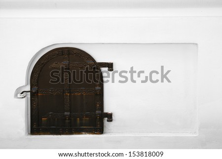 Old wooden door is hinged on white wall. Ancient entrance is armored with rusty iron stripes.