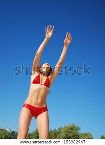Young woman is trying to catch anything. She is wearing red bikini. Her slender body is photographed from below. She is playing against the blue summer sky. She is acquiring a tan in the sun.