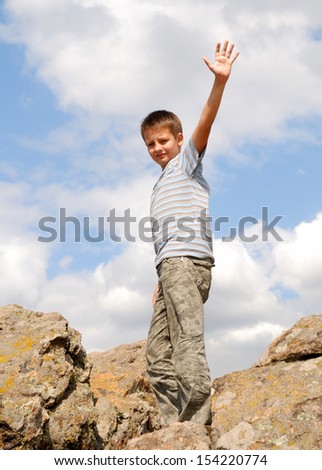 A series boy is standing between rocks against the sky, left arm is cocked for greeting