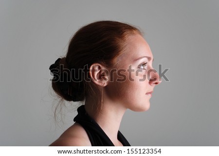Girl with red hair arranged on back of the head, half face, chain in small ear, expressive eyebrow and eye, long neck
