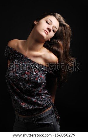Sexy teenage girl is standing in a haughty manner against the black background. Young woman is looking down on camera. Her head has been thrown back. Her dark long hair are flowing.