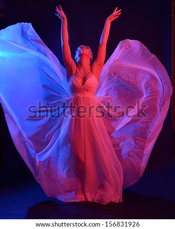 Blonde young woman is dancing in the dark. Her dress is streaming in the light of the blue and pink photo flashes. She is like a  butterfly.