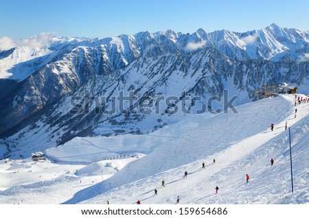 Skiers are sliding down snow-covered hill on skis at the Cirque du Lys. There is range of mountains (Soum de Mauloc) in the background. Winter Pyrenees is photographed at the Cauterets ski resort.