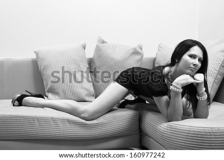 Sexy woman is lying on the sofa and looking at the camera. Her pose is seducing. She is wearing a short cocktail dress and shoes high-heeled.