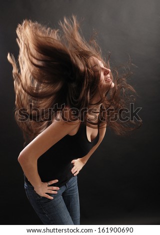 Young woman is shaking her head and happy laughing. Her dark long hair are soaring around hers.