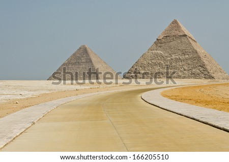 The concrete road turns to the Egyptian pyramids in the middle of barren desert under the blue sky.