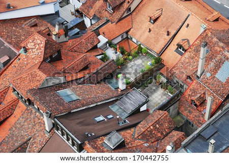 Red tiled roofs of townhouses tightly adjacent to each other. There are several roof gardens among them. The old city of Fribourg is photographed from above.