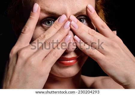 A young woman is covering her face with her hands. She is smiling and looking through the fingers.