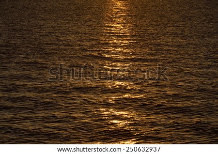 Light path is on the dark surface of the calm sea at sunrise.