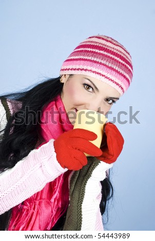 Beautiful brunette woman in pink winter clothes drinking a cup of hot drink and looking at you,right angle view
