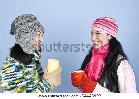 Friends women having a conversation,laughing together and enjoying a cup of hot drink to heat up over blue background