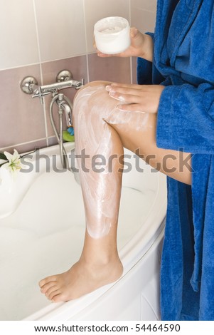 Woman rubbing cream on leg in bathroom