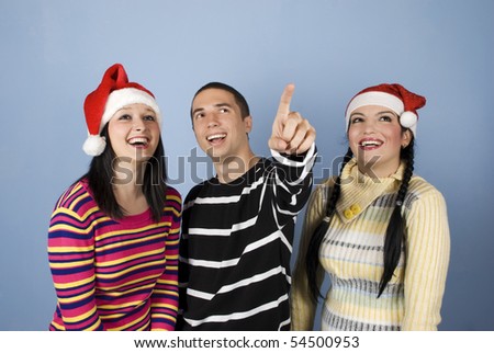 Happy young  Christmas  friends people with Santa hats  laughing together while the man pointing up somewhere towards the top right