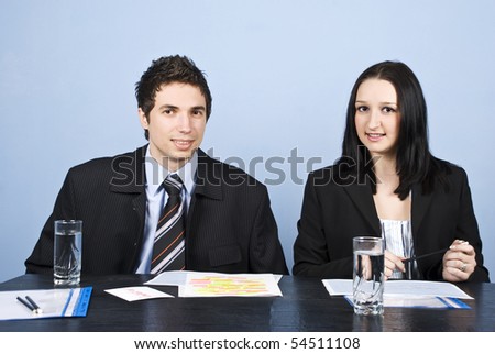 Two business people man and woman sitting at table with paperwork and having a discussion or an interview
