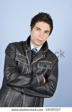 Modern business man posing in leather jacket and standing with arms folded in front of blue background