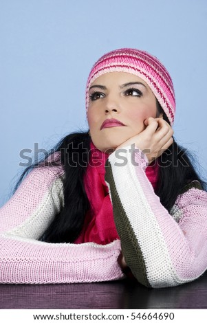 Beautiful woman in pullover and cap standing at table with hand at chin and dreaming or thinking and  looking up with a serious face