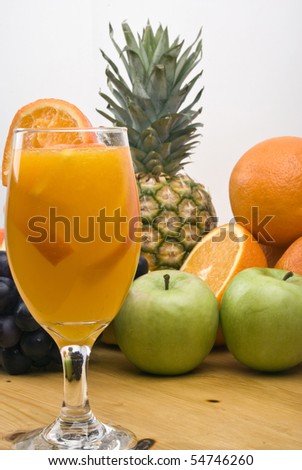 Glass of fresh orange juice in the foreground and fresh fruits in the background on wood table