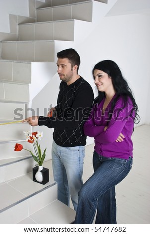 Young couple moving in new house,they measuring the stairs and planning together in an empty room with white wooden floor unfinished