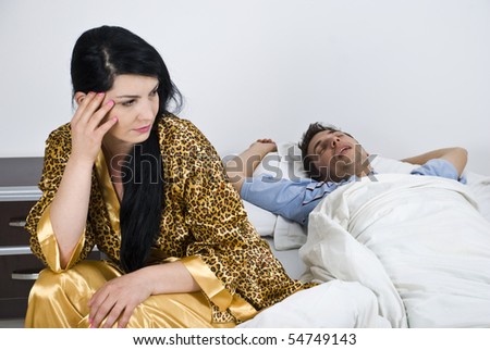 Young woman  awake sitting on bed having insomnia while her husband sleeping and snoring