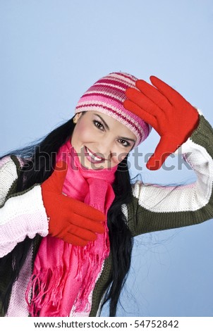 Happy young winter woman framing her face with hands in gloves and smiling,right angle view