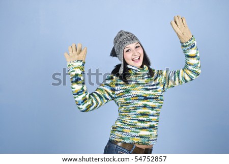 Excited winter girl with arms raised wearing sweater ,cap and gloves over blue background