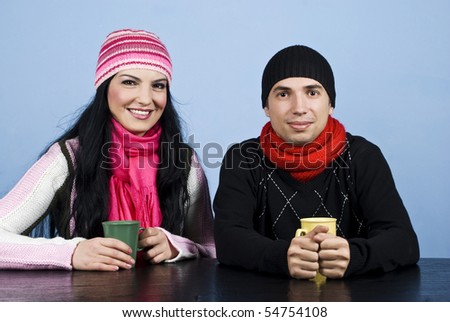 Happy couple in winter clothes standing at table and enjoying together a cup of hot drink and smiling