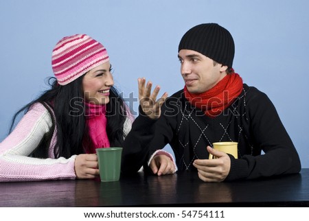 Young couple sitting at table and having a funny conversation,the man explaining something and gesturing and the woman laughing.They also enjoying a hot drink