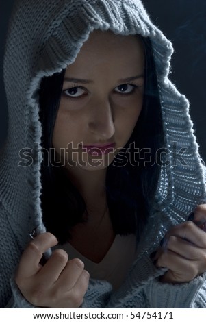 Portrait of girl with evil look wearing wool hood in darkness with smoke around