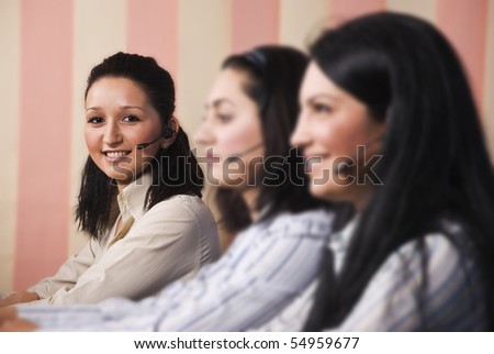 Three women customer service team  sitting in line at desktop ,focus on last young woman which looked at you and smiling