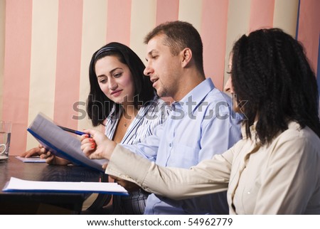 Group of business people sitting at desktop and having a conversation about some papers,one businesswoman showing something with pencil,vertical blinds background