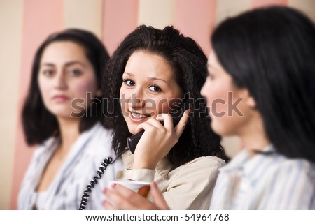 Three business women working in a office,focus on middle women that speaks by telephone and facing you with a smile
