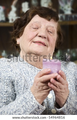 Older woman holding a big candle light and looking down while praying on her home