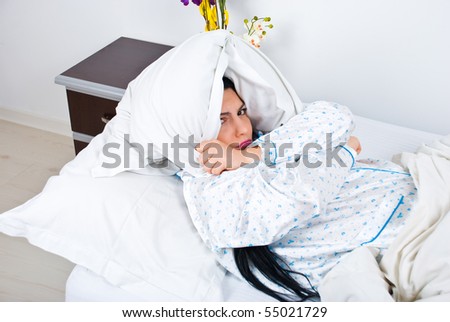 Sick sulky woman on bed with pillow on head and hands crossed do not wanna wake up or she can not sleep