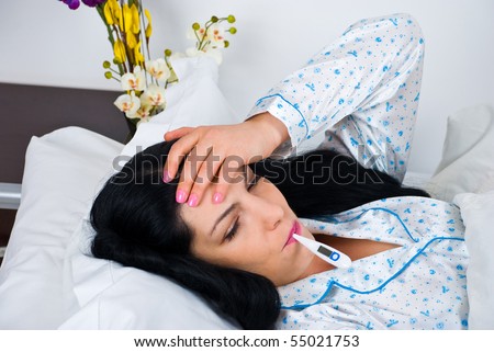 Sick woman having cold and fever and lying on bed checking temperature and holding hand on forehead