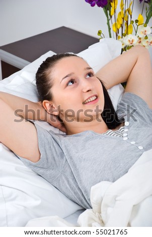Thinking young woman lying in bed and relaxing