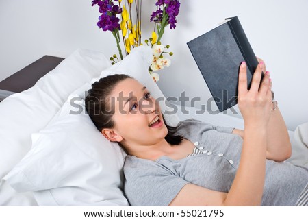 Woman lying on bed reading a captivate book and looking surprised