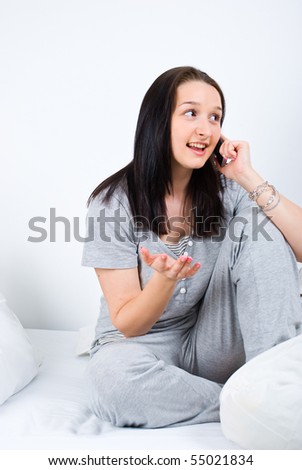 Young woman sitting on bed and having an conversation at phone mobile,she smiling,looking away and gesticulate with hand trying to explain something