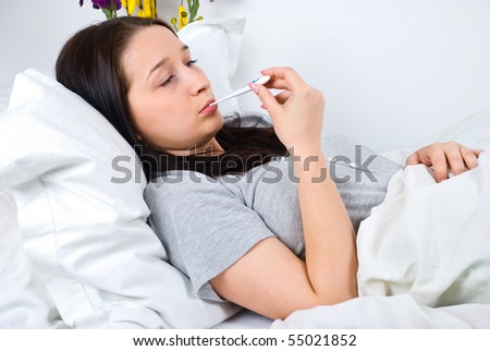 Sick young woman having cold and checking temperature in bed